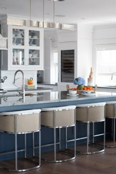 a kitchen with blue counter tops and white cabinets, along with bar stools that have beige upholstered seats