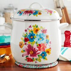 a large white pot with colorful flowers painted on the front and sides sitting on a wooden table