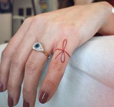 a woman's hand with a bow tattoo on her left thumb and an evil eye ring