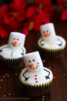 three frosted cupcakes with snowmen on them sitting on a wooden table