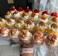 cupcakes with white frosting and toppings are displayed in a display case