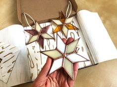 a hand holding a star shaped ornament in front of a box on a table