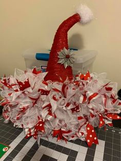 a red and white christmas hat on top of a pile of ribbons with a green box in the background