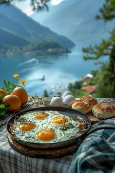 eggs and pastries are sitting on a picnic table overlooking the water with mountains in the background