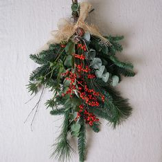 a christmas wreath hanging on the wall with red berries and greenery attached to it