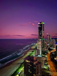 an aerial view of a city at night with the ocean in the foreground and buildings lit up