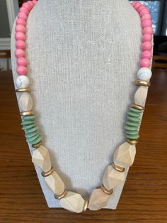 a necklace with pink, white and green beads on a mannequin head stand