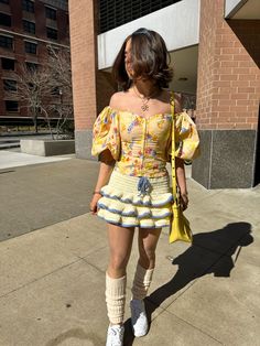 a woman walking down the street wearing a yellow dress and knee high socks with white shoes