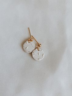 two white earrings are hanging from gold earwires on a white surface with light colored fabric