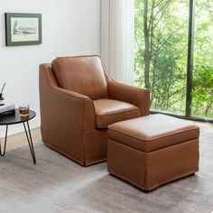 a living room with a chair and ottoman next to a large window overlooking the woods