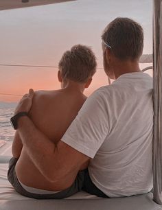 two men sitting on the back of a boat watching the sun go down over the ocean