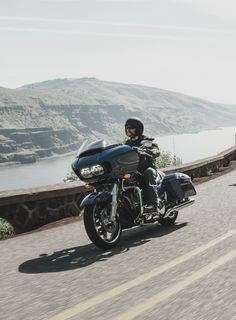 a man riding on the back of a motorcycle down a road next to a lake