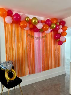 balloons and streamers are hanging from the ceiling in front of an orange curtain with gold fringes