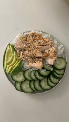 a white plate topped with cucumber and salmon next to sliced avocado