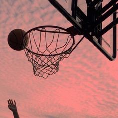 a basketball going through the hoop with someone's hand reaching up to grab it