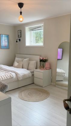 a large white bed sitting in a bedroom next to a dresser and mirror on top of a hard wood floor