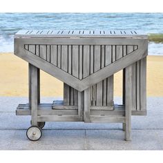 an outdoor table with wheels on the sidewalk next to water and beach in the background