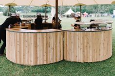 people are sitting under an umbrella in the grass near some tables and chairs with food on them