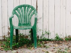 a green plastic chair sitting in front of a white wooden fence with ivy growing on it