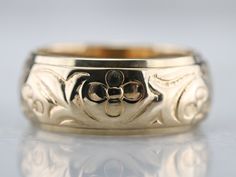 a gold wedding ring with an ornate design on the outside and inside, sitting on a reflective surface