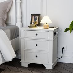 a white nightstand with two drawers next to a bed