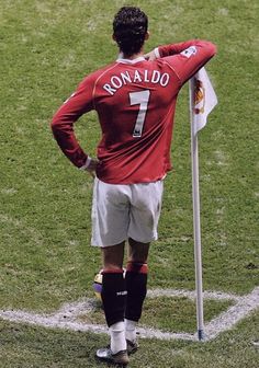 a man standing on top of a soccer field next to a flag and wearing a red shirt