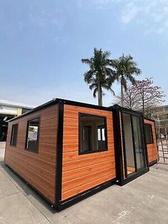 a small wooden building sitting on top of a parking lot next to a palm tree