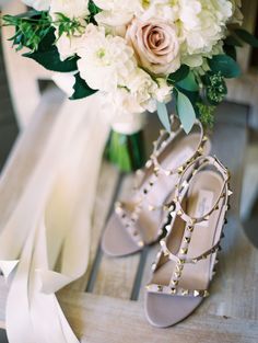 a bouquet of white flowers and high heeled shoes on a wooden table with ribbons