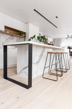 a kitchen with white marble counter tops and black metal barstools in the center