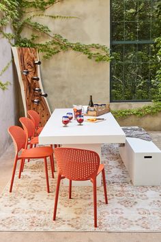 an outdoor dining table with orange chairs and bottles of wine on it, next to a white bench