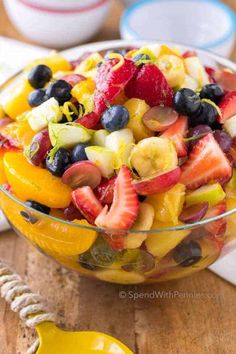 a fruit salad in a glass bowl on top of a wooden table next to a napkin