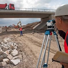 a construction worker looking at the ground with a tripod in front of him and another man standing next to it