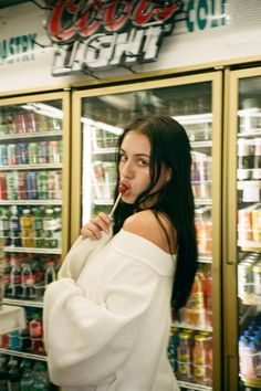 a woman standing in front of a store filled with drinks and sodas, brushing her teeth