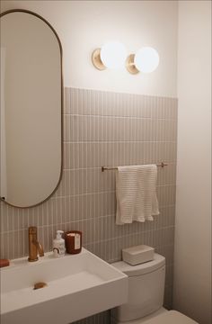 a white toilet sitting next to a bathroom sink under a large mirror and two lights