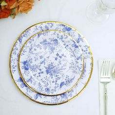 two blue and white plates sitting on top of a table next to silver utensils