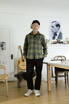 a man standing in front of a table with a dog on it and a guitar behind him