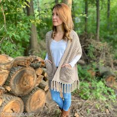 a woman standing next to a pile of logs in the woods wearing a shawl