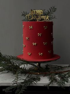 a red and gold christmas cake with pine branches on the side, topped by merry congratulations topper