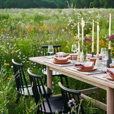 a table set with plates and candles in the middle of a field full of wildflowers