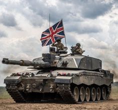 a british army tank driving down a dirt road with a flag on it's roof