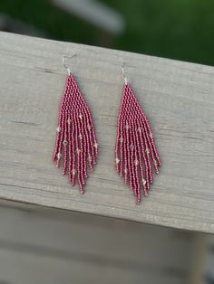 the pink beaded earrings are hanging from hooks on a wooden bench outside with grass in the background