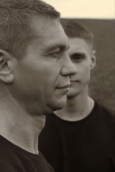 two young men standing next to each other in a black and white photo, one looking at the camera