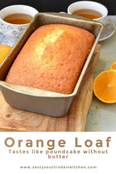 an orange loaf cake in a pan on top of a cutting board next to two cups of tea