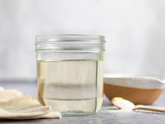 a glass jar filled with white liquid next to a wooden spoon and cloth on a table