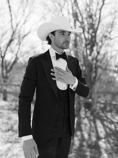 a man in a suit and hat is posing for a black and white photo with trees in the background