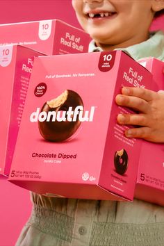 a young boy holding three boxes of donuttul chocolate covered doughnuts