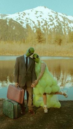 a man and woman dressed in frog costumes standing next to each other with suitcases