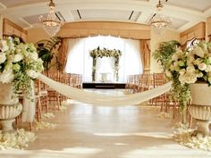 an aisle decorated with white flowers and greenery for a wedding ceremony in front of a large window