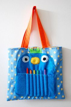 a blue tote bag with an orange handle hanging on the wall next to a white wall