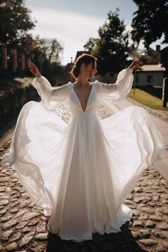 a woman in a white dress standing on a cobblestone road with her arms outstretched